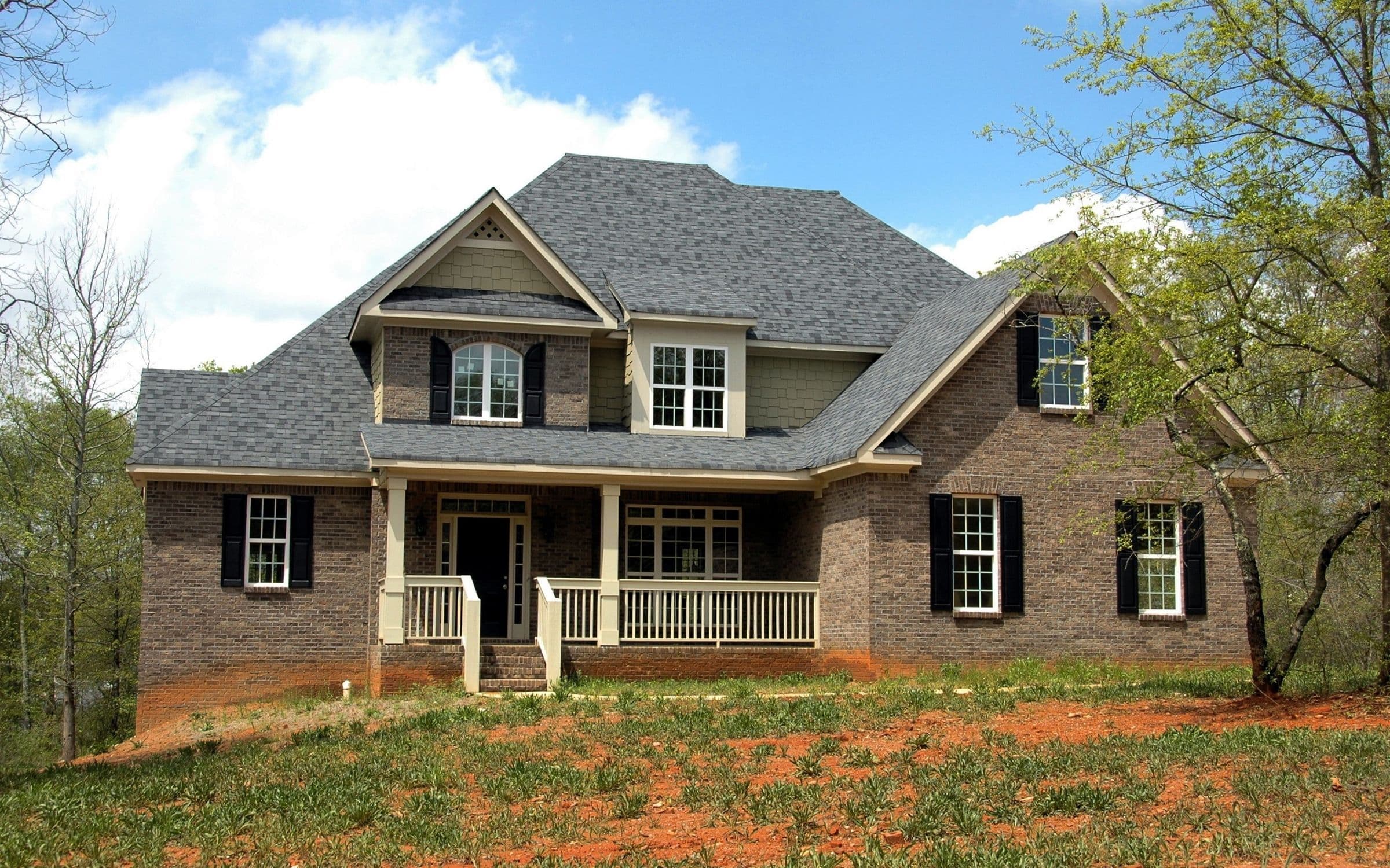Newly built brick two-story home with a front porch and black shutters on red-clay ground