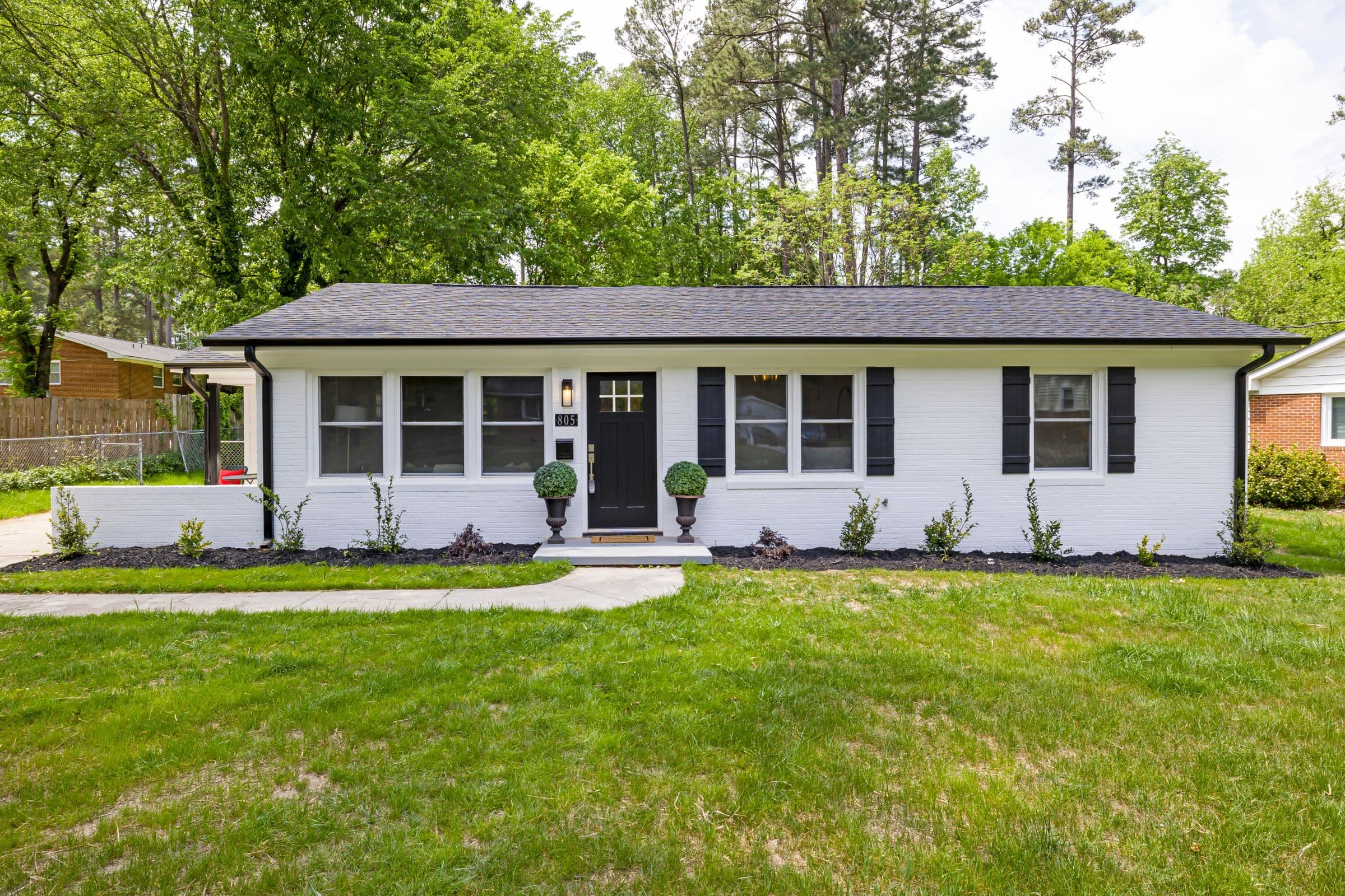 Painted white brick ranch house with black shutters and a front lawn
