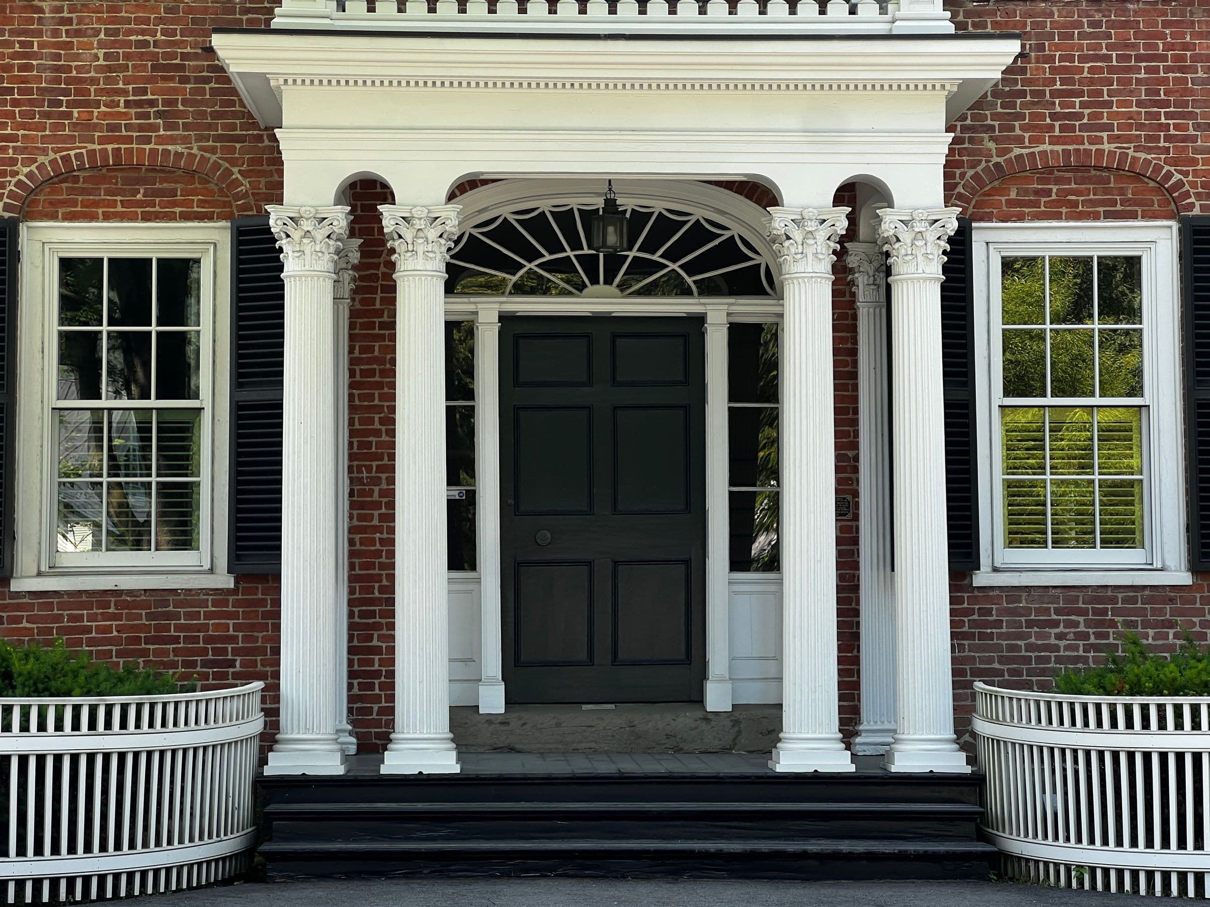 Historic red brick entrance with white fluted columns, fanlight and black shutters