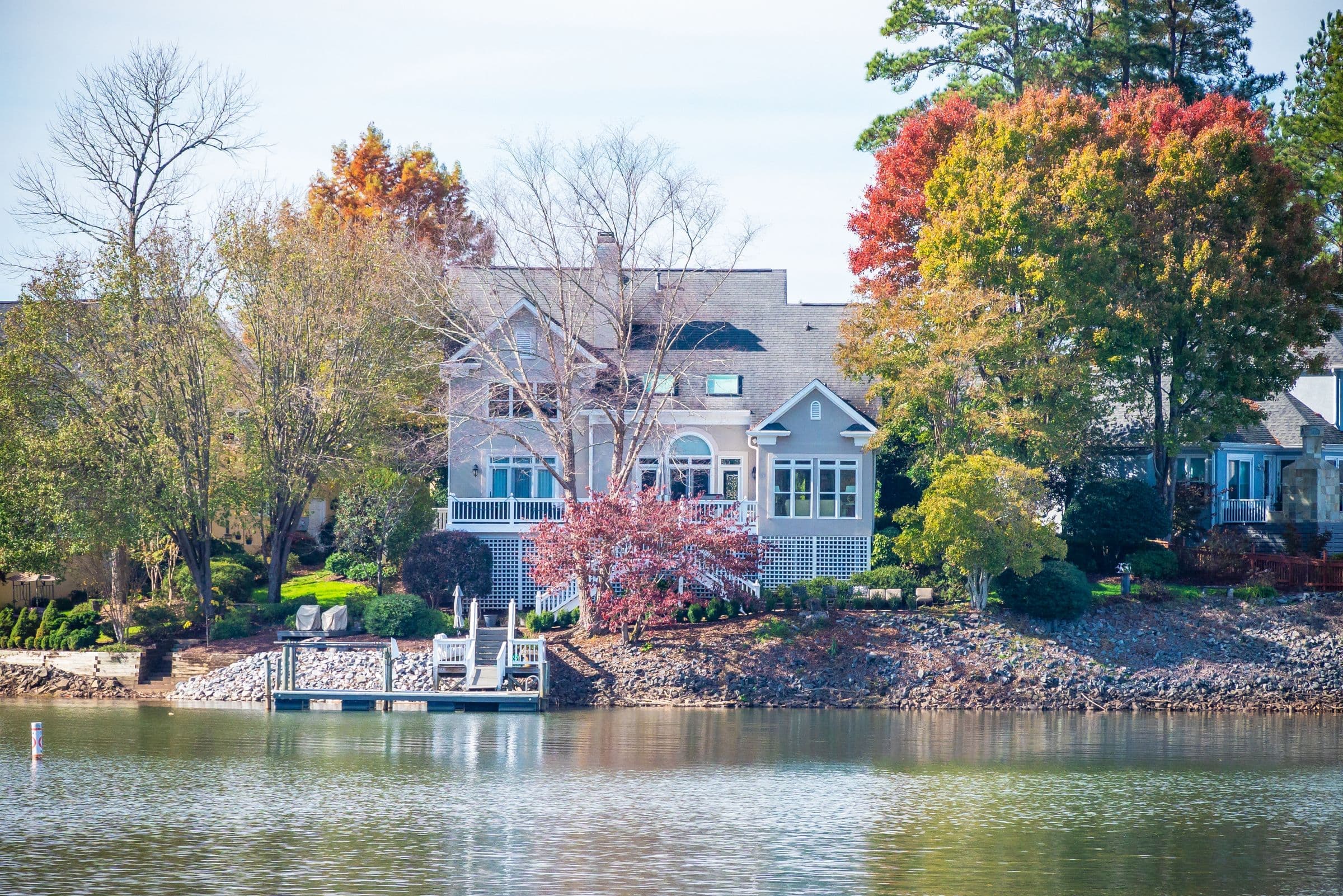 Large lake house with a white dock and autumn trees reflected in the water