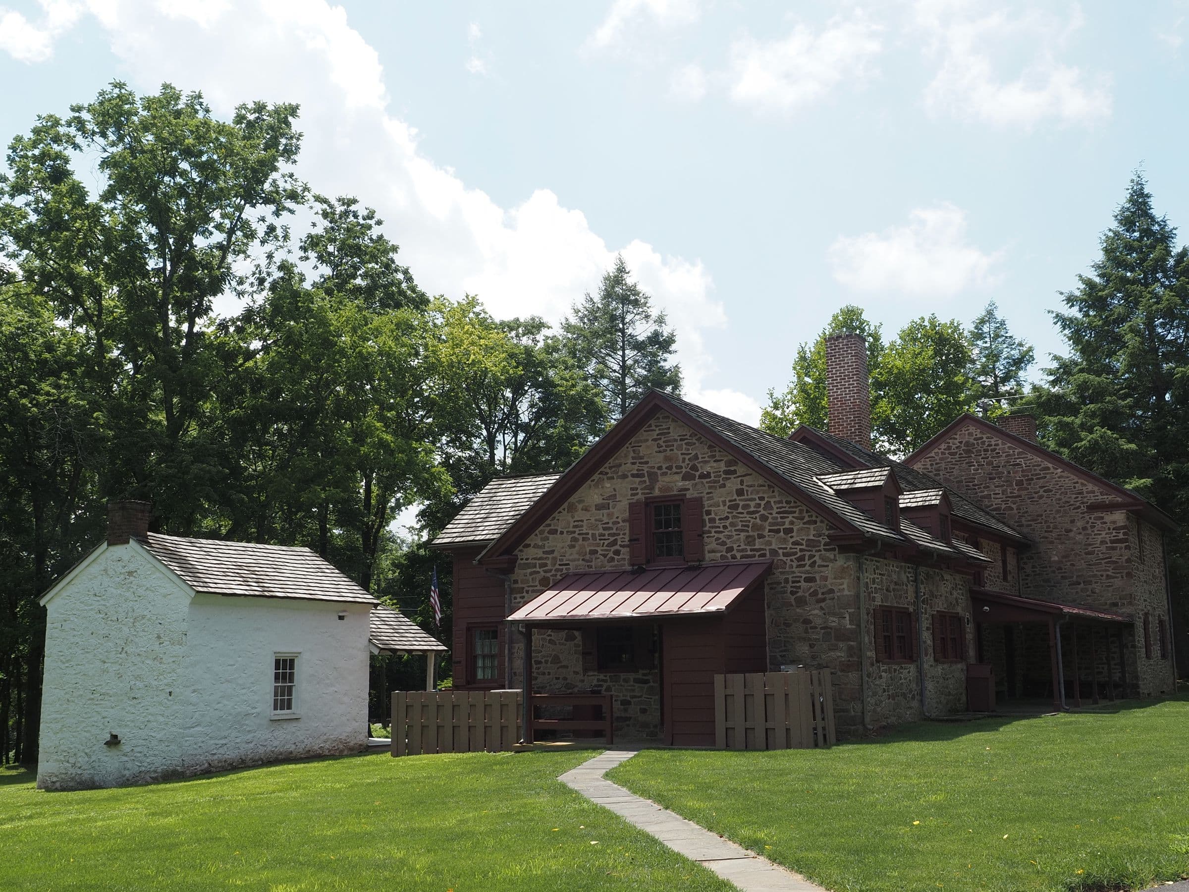 Historic fieldstone house with a whitewashed outbuilding on a green lawn under tall trees
