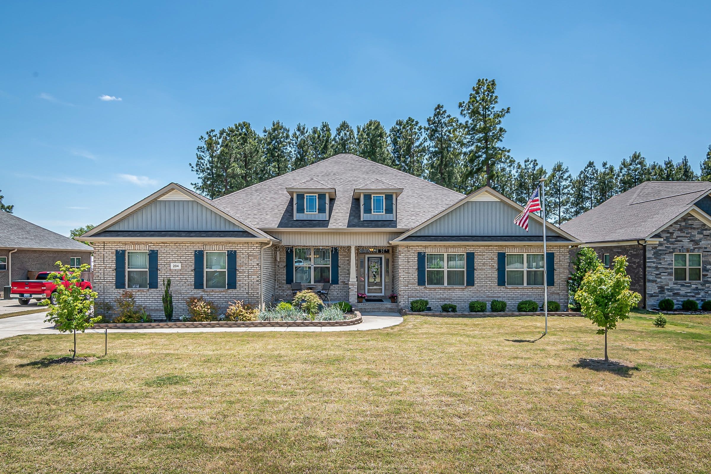 Newer brick and siding ranch home with dormers and an American flag on a wide lawn