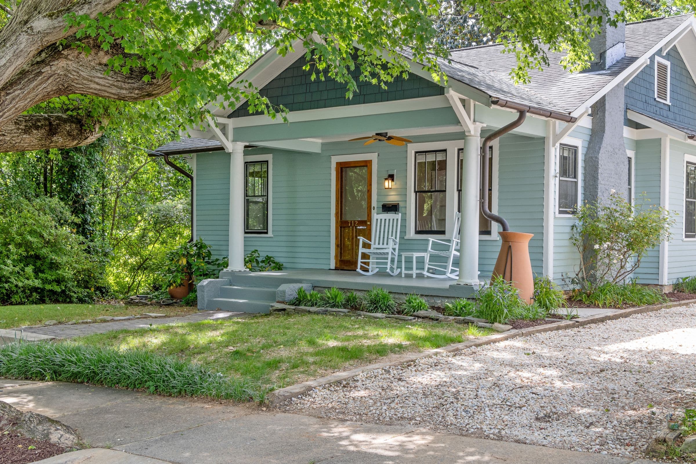 Small sage-green bungalow with a front porch and white rocking chairs