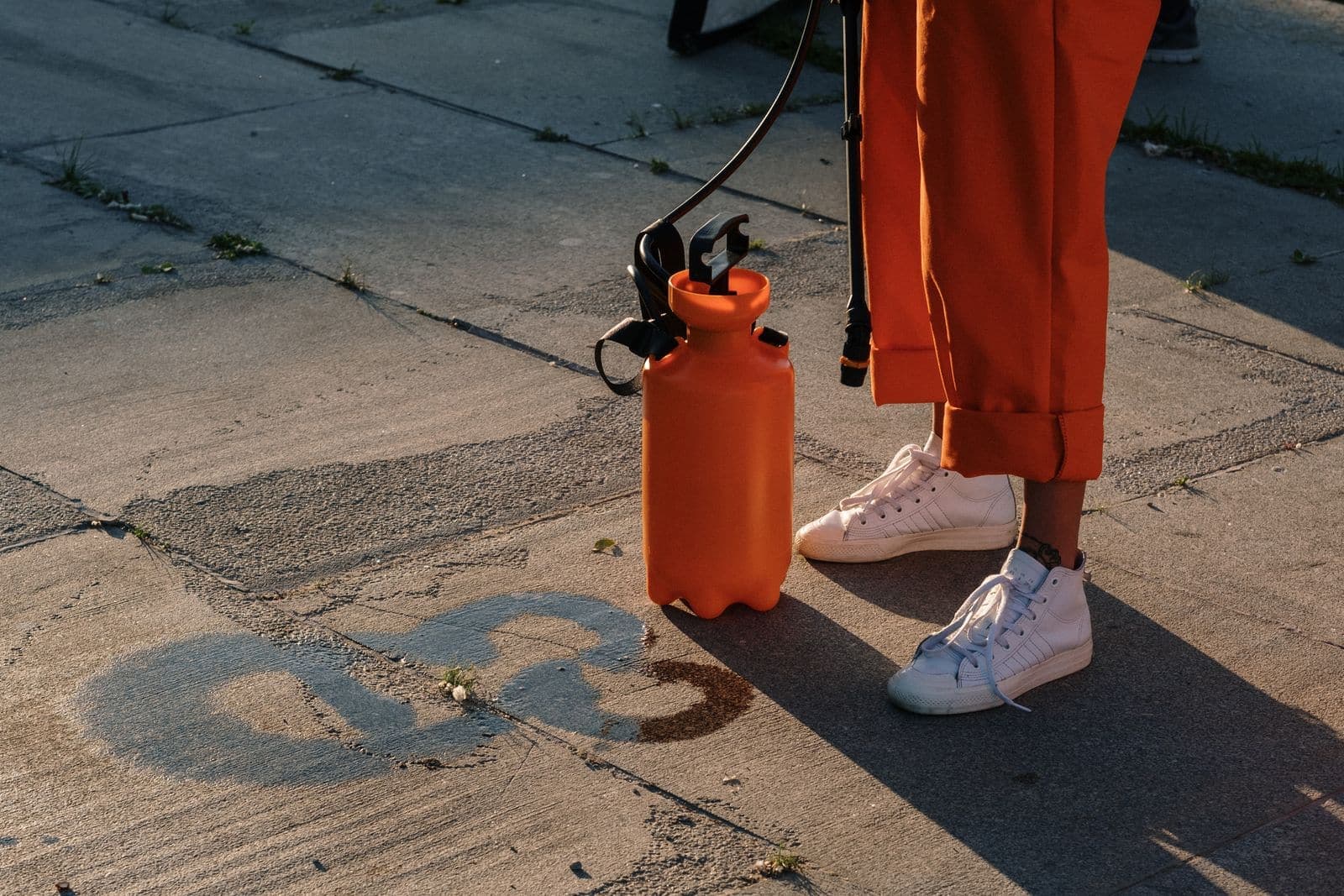 Pump sprayer on concrete pavement beside a worker in orange coveralls