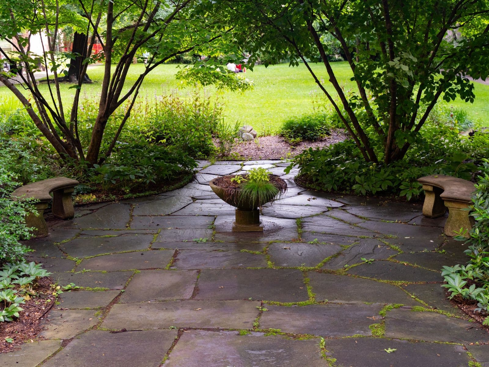 Flagstone patio with stone benches surrounded by garden trees