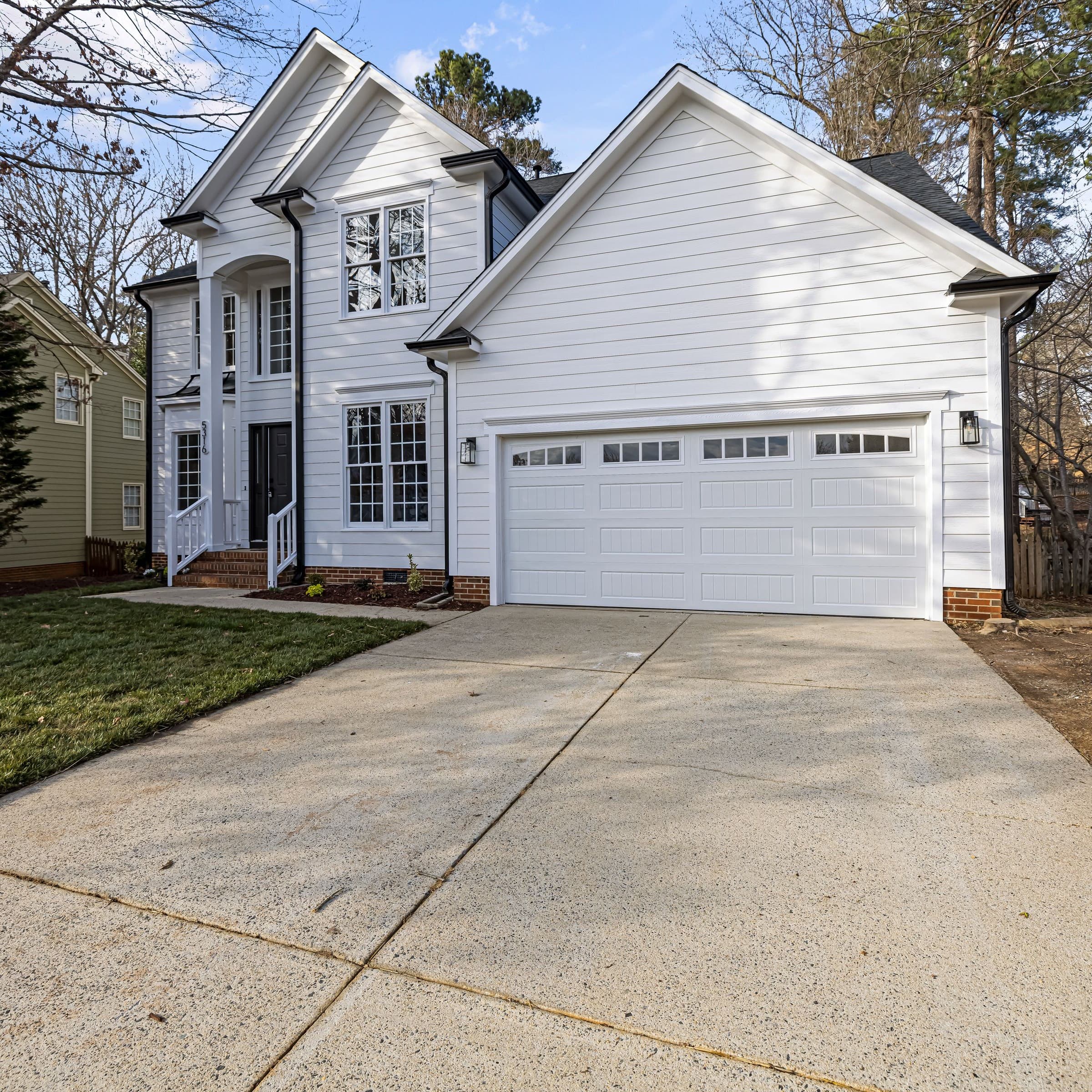 Bright concrete driveway after driveway cleaning, in front of a white two-story home