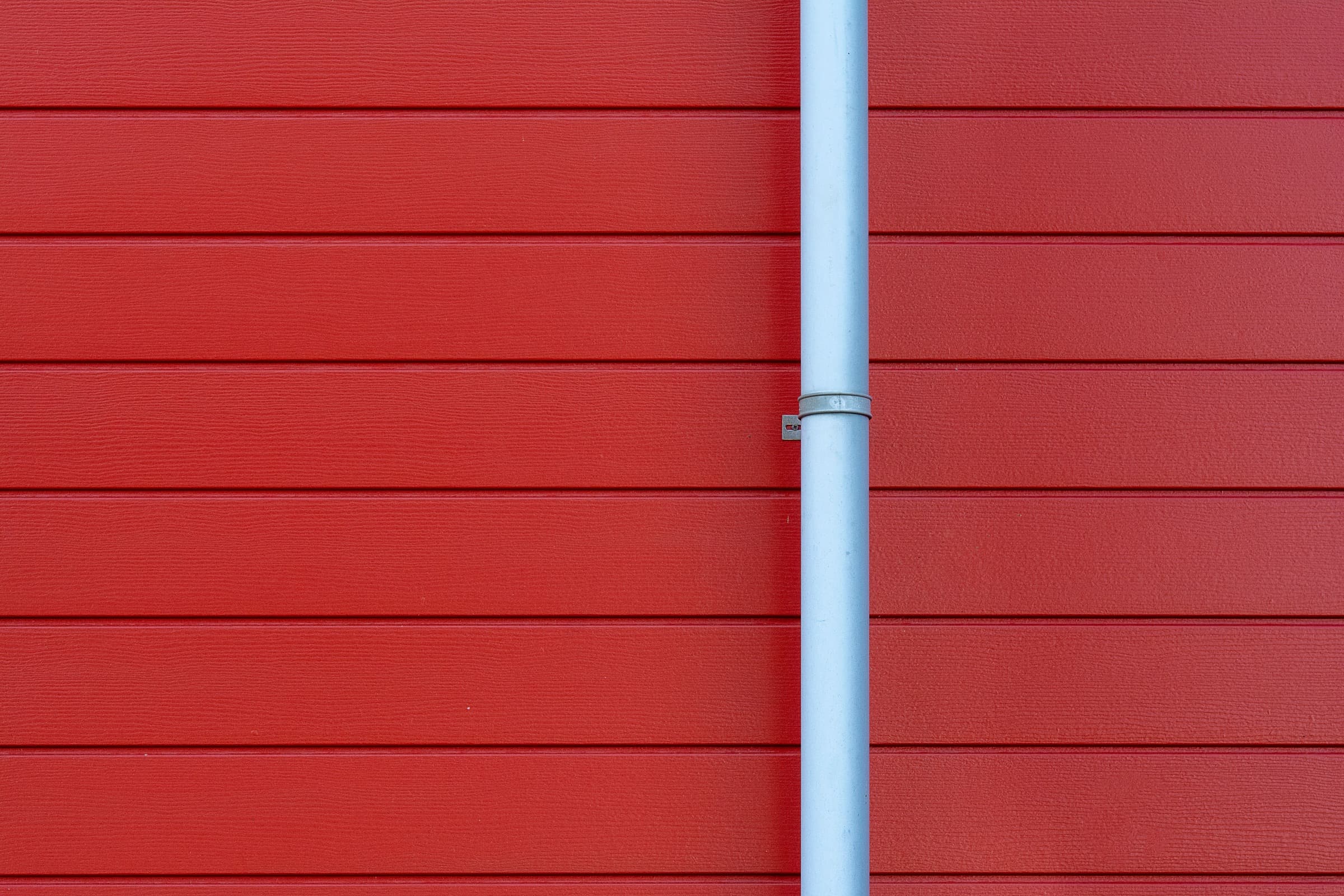 White downspout on clean red siding, part of the gutter line that gutter cleaning keeps flowing